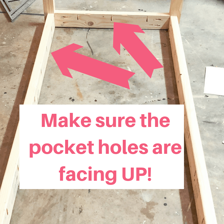 The base of a table flipped upside down on the floor with text overlay that reads \"Make sure the pocket holes are facing UP\" with arrows pointing at the pocket holes.