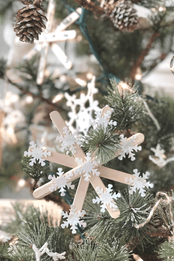 Popsicle stick snowflake ornament hanging on a Christmas tree with twine.