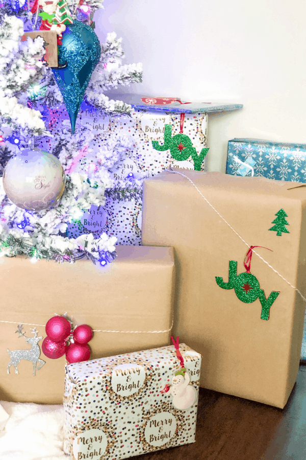 Christmas presents under a white Christmas tree with ornaments and lights.