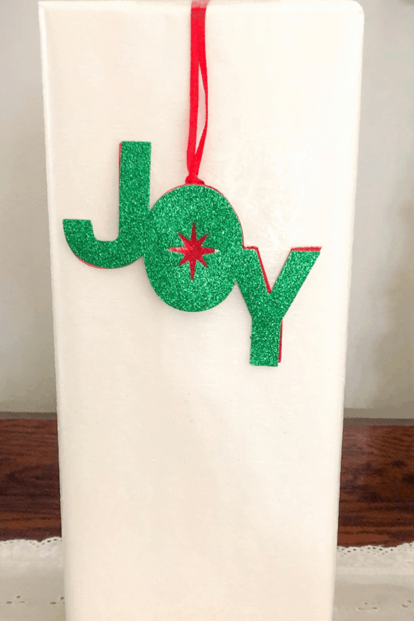 A Christmas present wrapped in white paper with green and red \"Joy\" cutout.