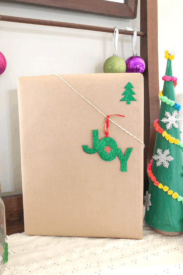 A rectangular Christmas present covered in butcher paper and decorated with an ornament and twine.