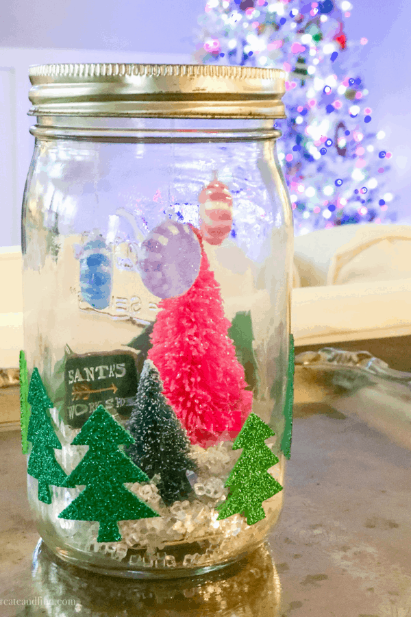 A homemade mason jar snow globe with a mini Christmas tree farm inside.