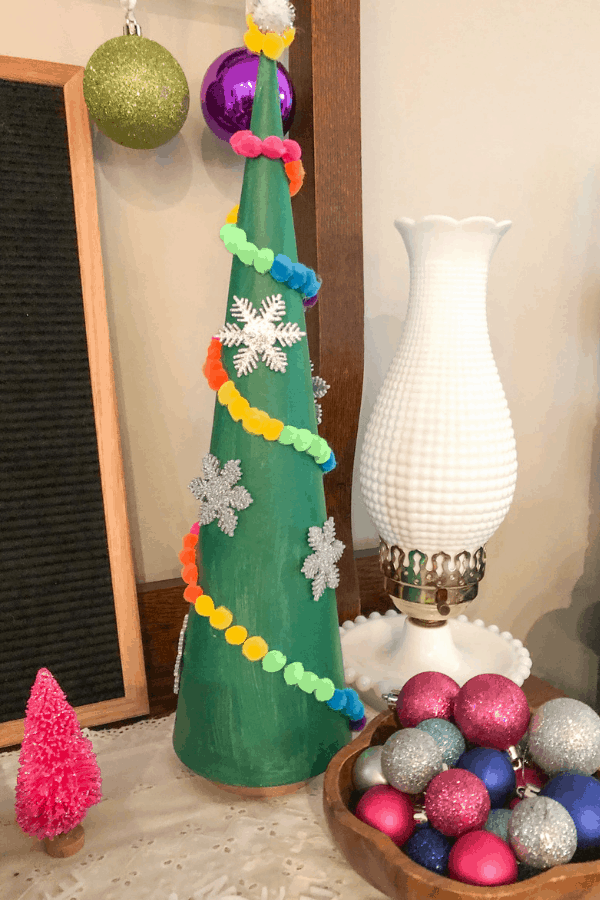 A green Christmas tree cone decorated with cotton ball garland and silver snowflakes.