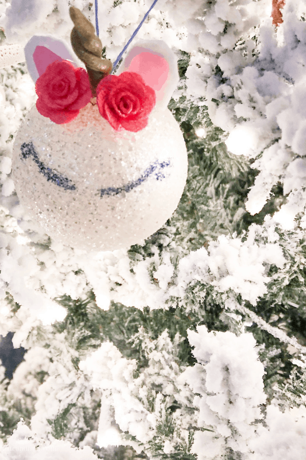 Close-up of a homemade unicorn ornament with a flower crown hanging from a Christmas tree.