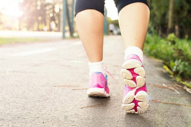 The feet of a woman running in pink shoes on a sidewalk.