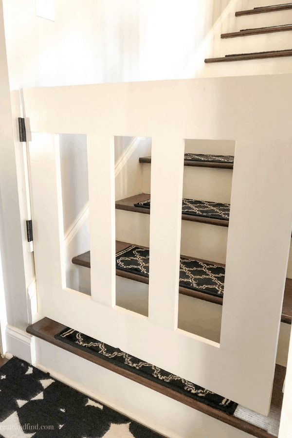 Close-up of a white baby gate attached to the wall in front of wood stairs.