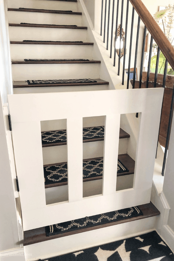 A white baby gate closes off the bottom of stairs in a home.