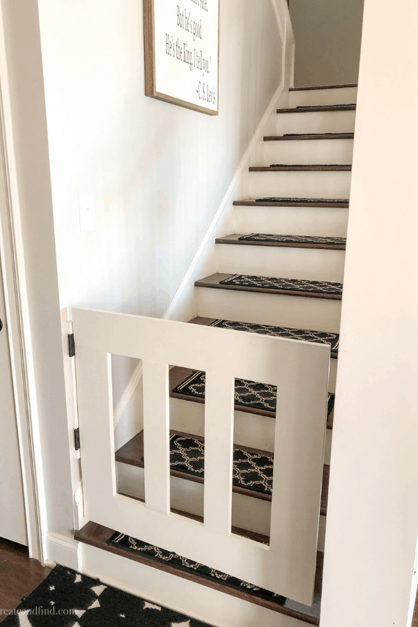 A white baby gate blocks the entrance to the bottom of wood stairs.