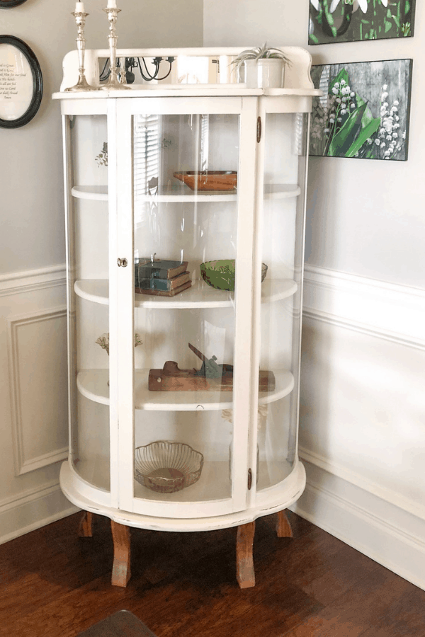 A white farmhouse curio cabinet with glass and décor pieces inside.