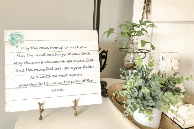 A wooden sign with cursive writing on a stand, sitting on a side table with plants.