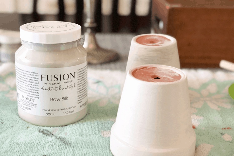 Two painted clay pots turned upside down on a table with a jar of Fusion paint.