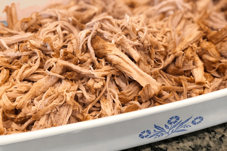 Close-up of shredded pork tenderloin in a white casserole dish with a blue floral design.