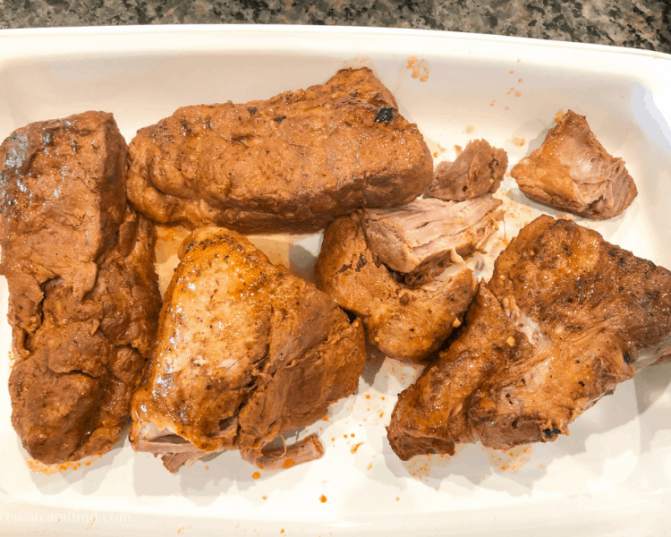 Hunks of cooked pork tenderloin in a white casserole baking dish on a granite countertop.