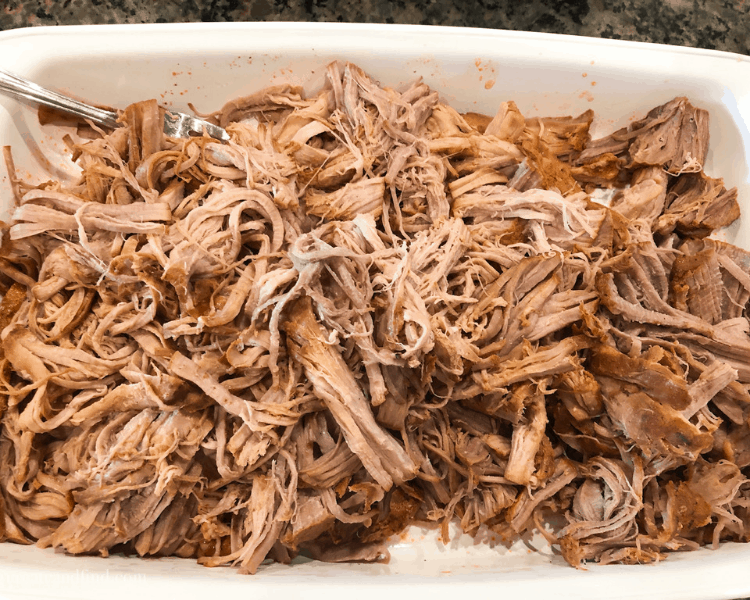 Over-head shot of shredded pork tenderloin in a white baking dish on a kitchen countertop.