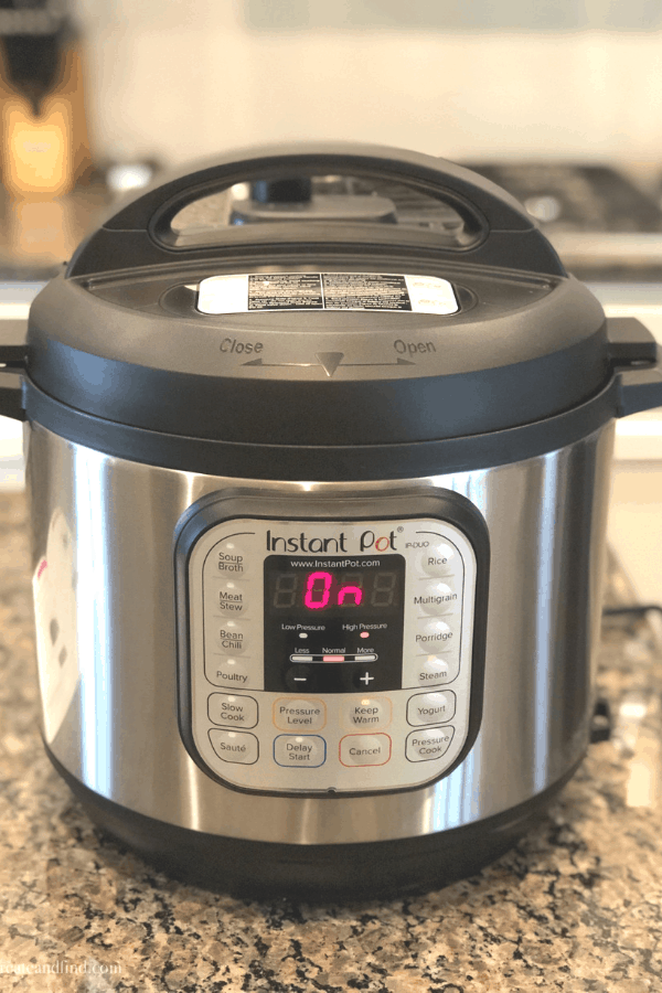 An instant pot in \"on-mode\" on a granite countertop.