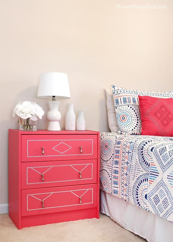 A bed with a colorful blue and coral bedspread with a coral-colored nightstand and white nightstand décor.