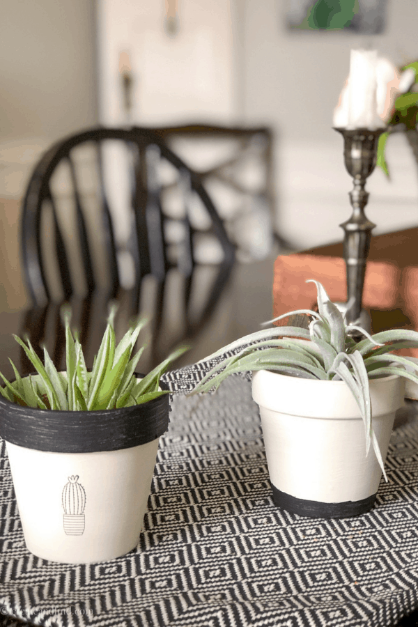 Black and white potted plants on a dining room table with a black and white tablecloth. 