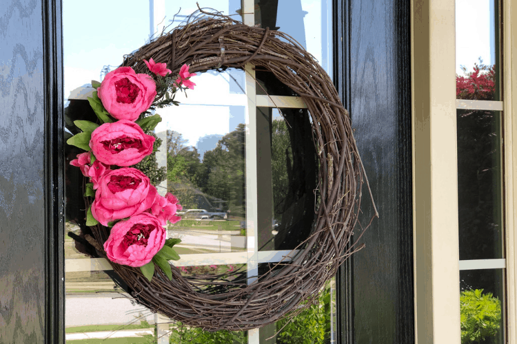 A summer wreath with pink peonies hangs from the front door of a home.