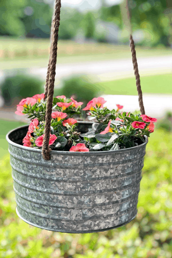 Pink calibrachoa flowers in a hanging metal planter on a front porch.