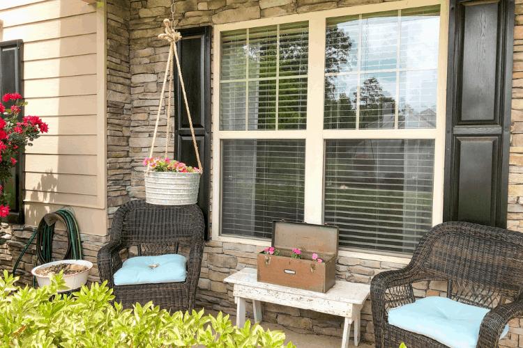 A front porch with wicker chairs and planters with pink flowers.