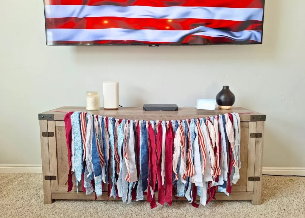 Red, white, and blue fabric strip American flag garland on the front of an entertainment center.