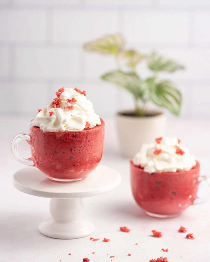 Two red velvet mug cakes with whipped cream on top.