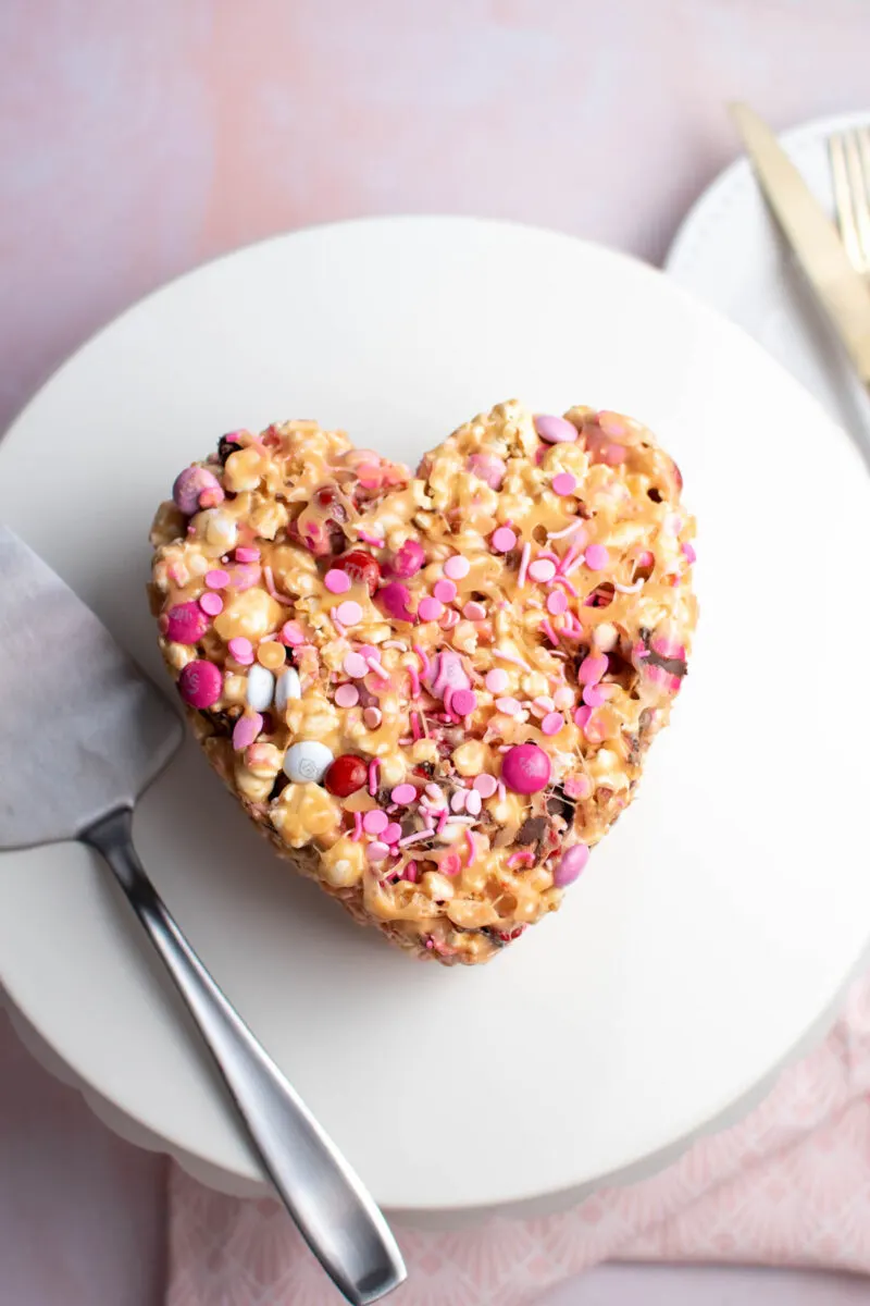 Heart-shaped popcorn cake with Valentine's Day sprinkles on a white plate.