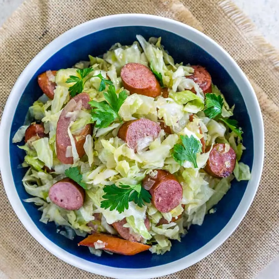 Kielbasa and cabbage stir fry in a large white and blue bowl.