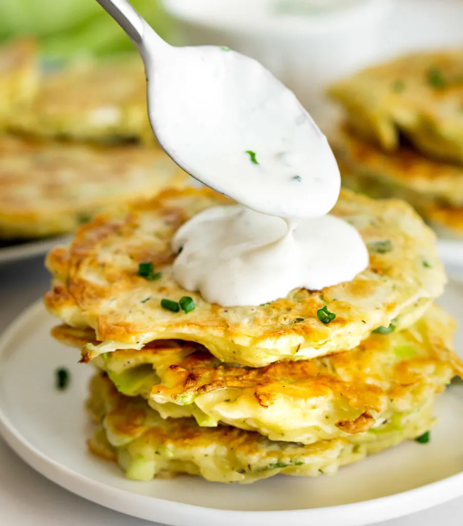 Stack of cabbage fritters with cream spooned on top on a white plate.