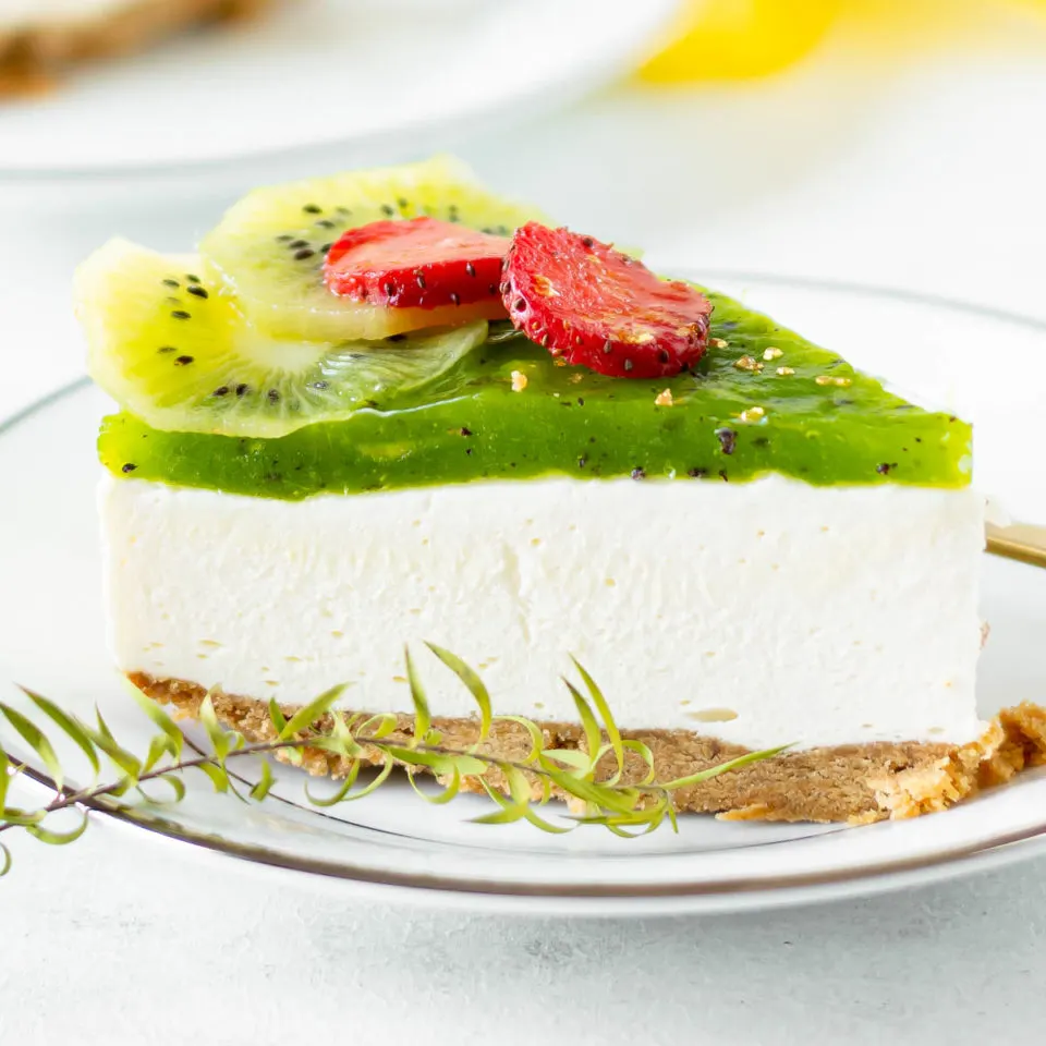 Slice of kiwi cheese cake with graham cracker crust on a white plate.