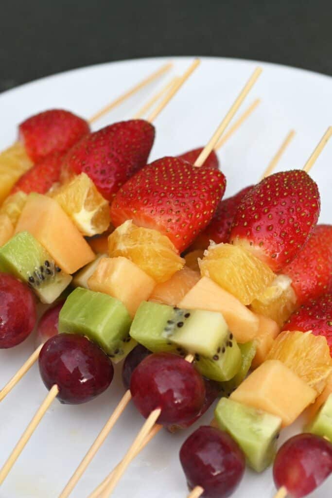 Rainbow fruit skewers on a white plate.
