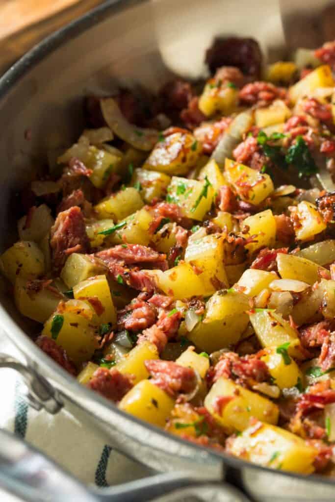 Corned beef and hash in a large metal skillet with green garnish.