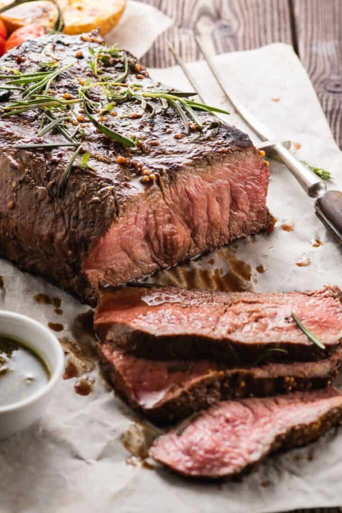 Sliced Irish beef roast next to a bowl of aus jus.