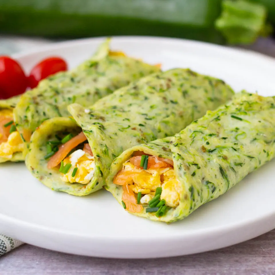 Three breakfast zucchini wraps on a white plate with grape tomatoes.