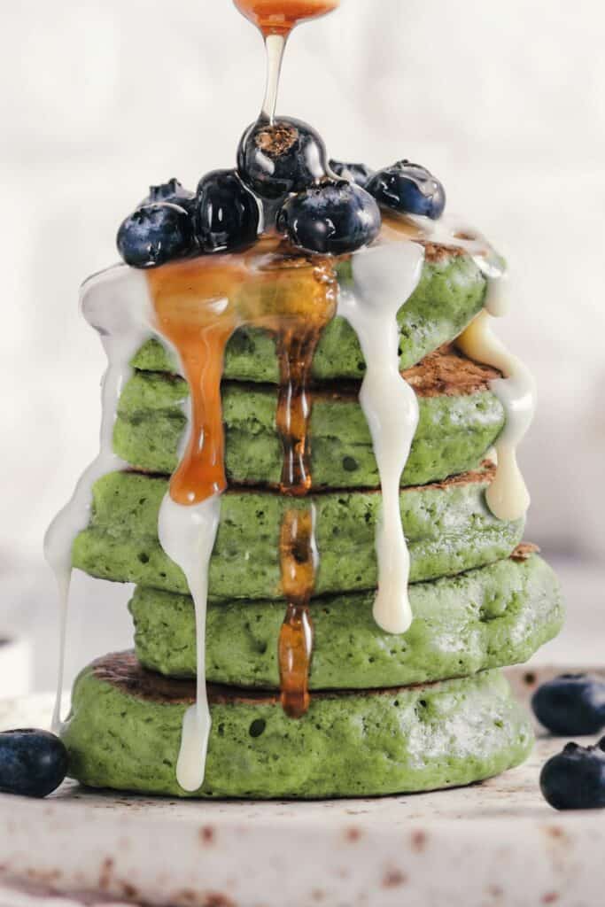 A stack of fluffy green pancakes with blueberries and cream on top.
