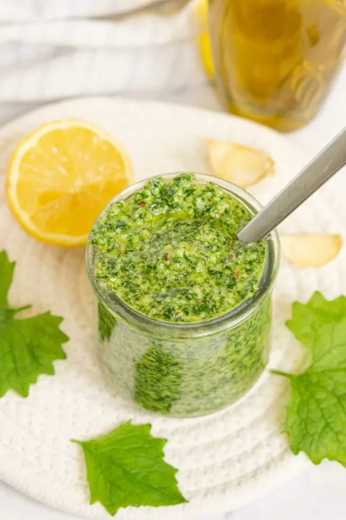 Garlic mustard pesto in a glass jar with a spoon inside.
