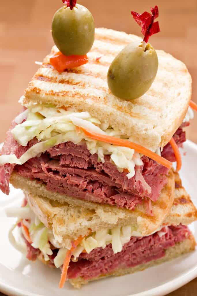 Rueben sliders with green olives skewered on top with toothpicks.