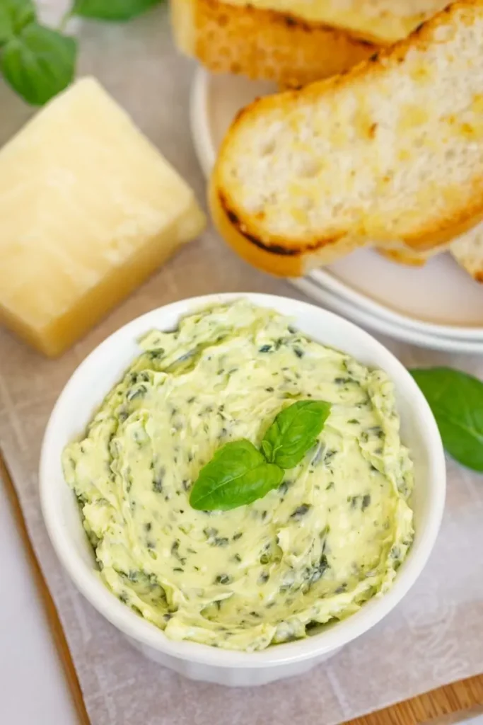 Pesto butter in a white bowl with green garnish next to bread.