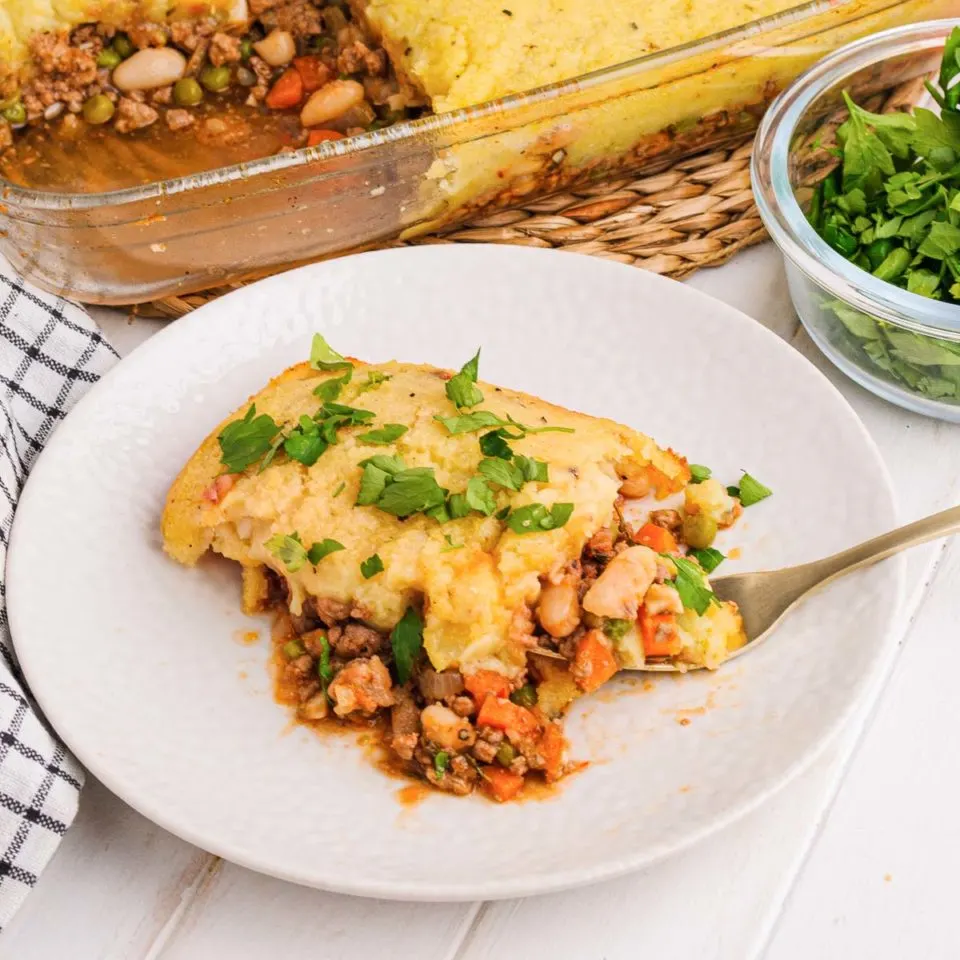 Shepherd's pie with white beans on a white plate next to the casserole dish.