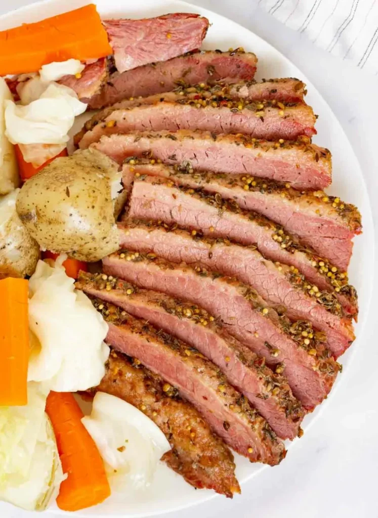 Corned beef on a white plate with potatoes and carrots.
