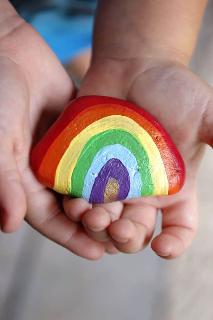 A child holds a rock painted to look like a rainbow.