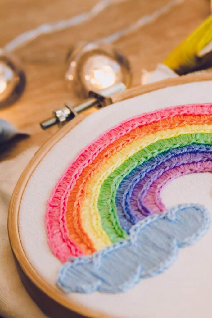 Needlepoint rainbow design with blue clouds.