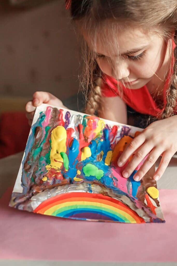 A child showing off a fingerpainted rainbow art project.
