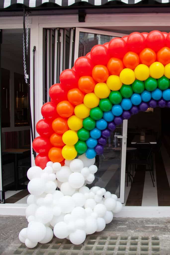 A rainbow balloon arch in front of patio doors outside.