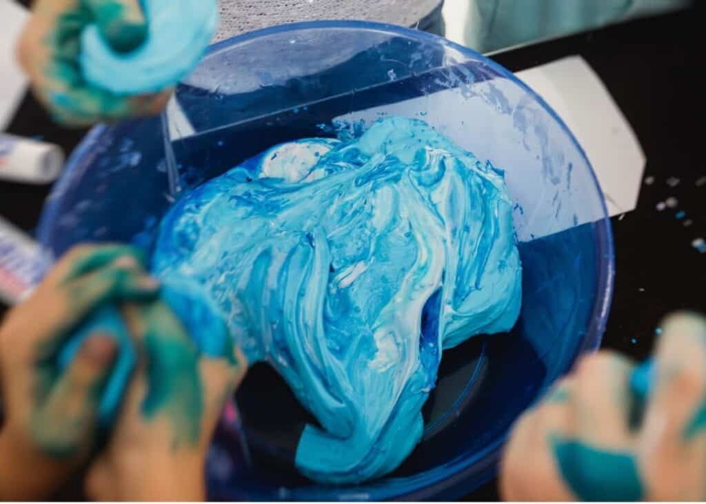 A child mixing blue and white slime in a blue bowl.