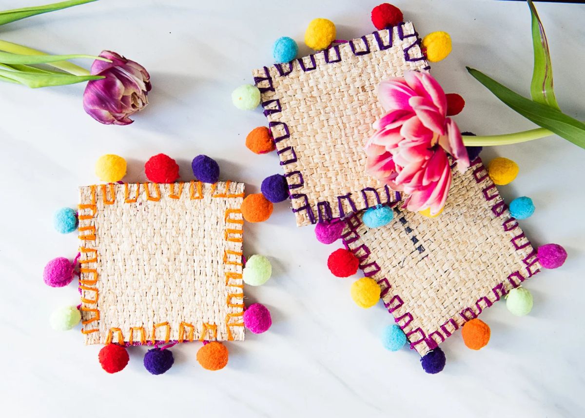 Colorful burlap pom pom coasters with spring flowers on a white background.