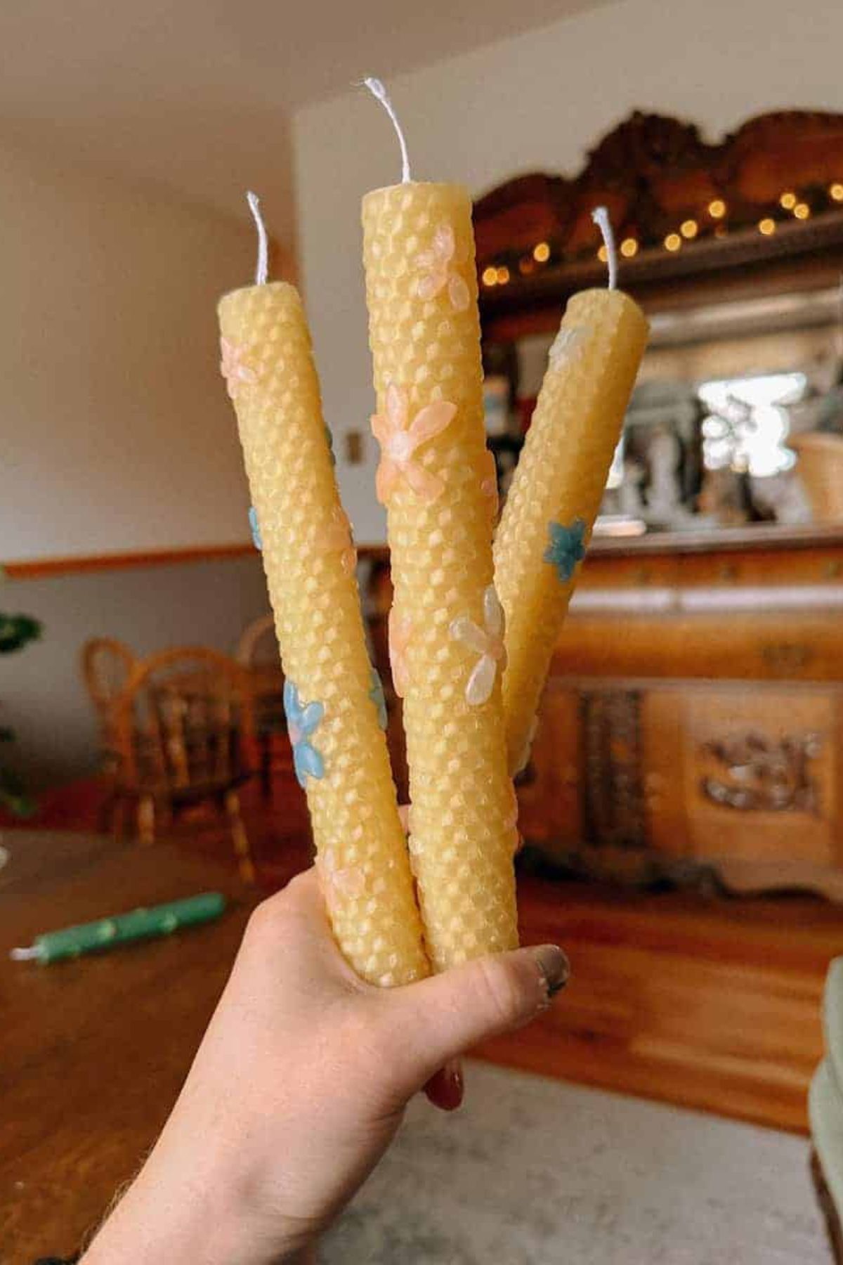A woman holds three rolled beeswax candles with mini flower designs.