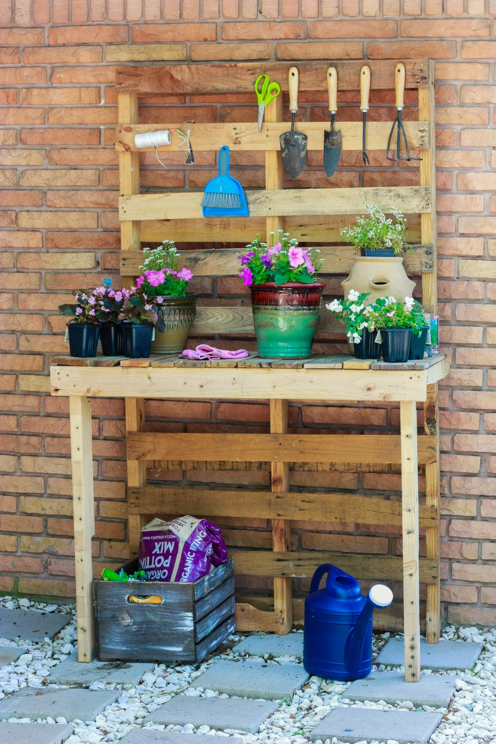 A DIY pallet wood potting station against a brick wall outside.