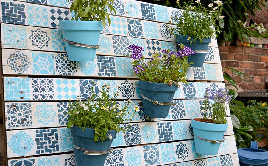 A blue-patterned plant wall with hooks holding small planter pots.